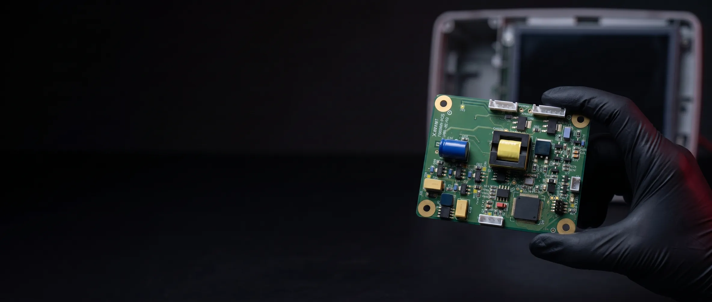 The Xenith module board held in a gloved hand over a dark engineering bench, an opened patient monitor behind